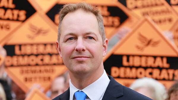 Richard Foord stood in front of a wall of orange Liberal Democrat posters